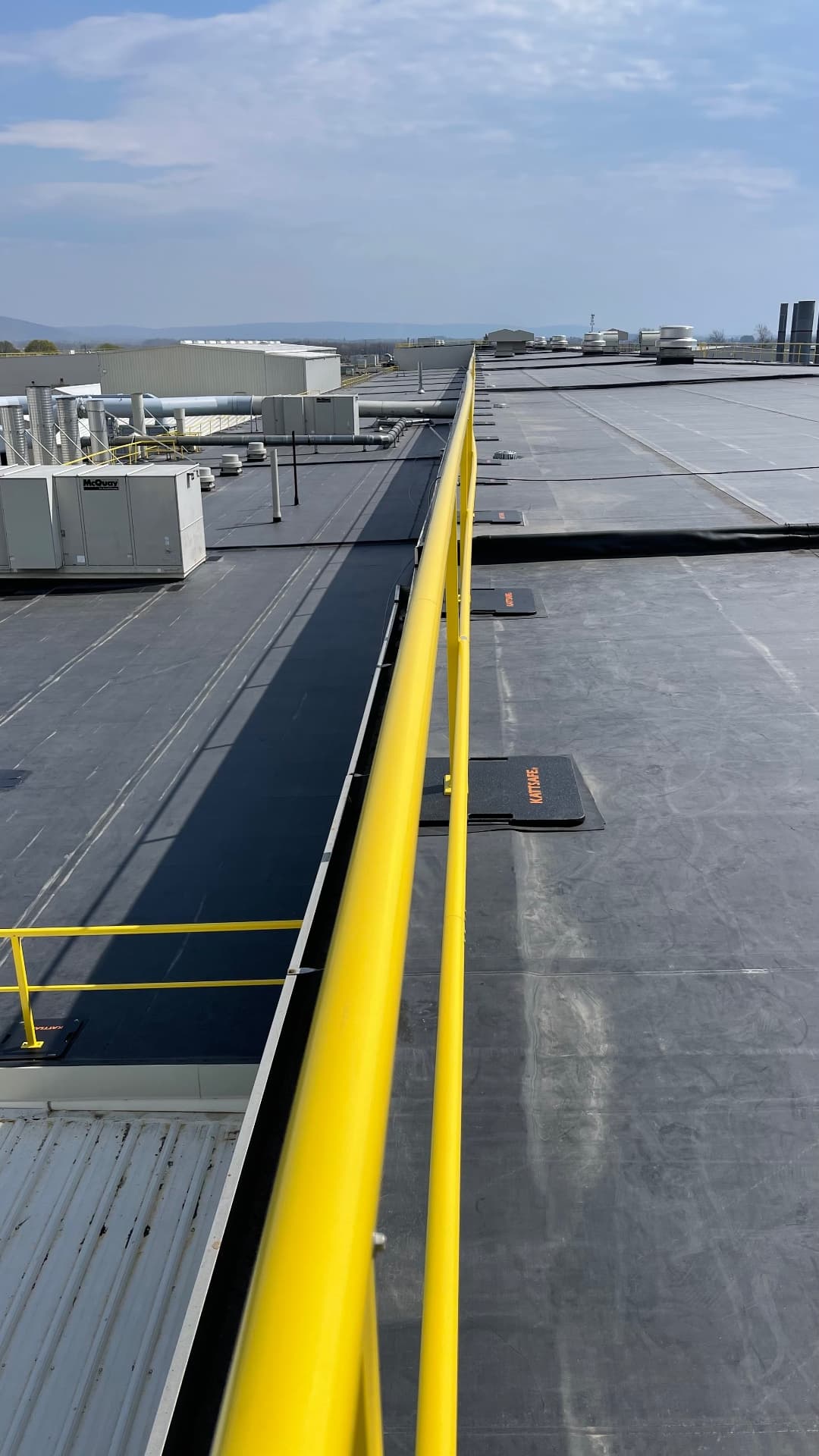 Completed EPDM commercial roof with yellow OSHA safety rail and large rooftop mechanical equipment