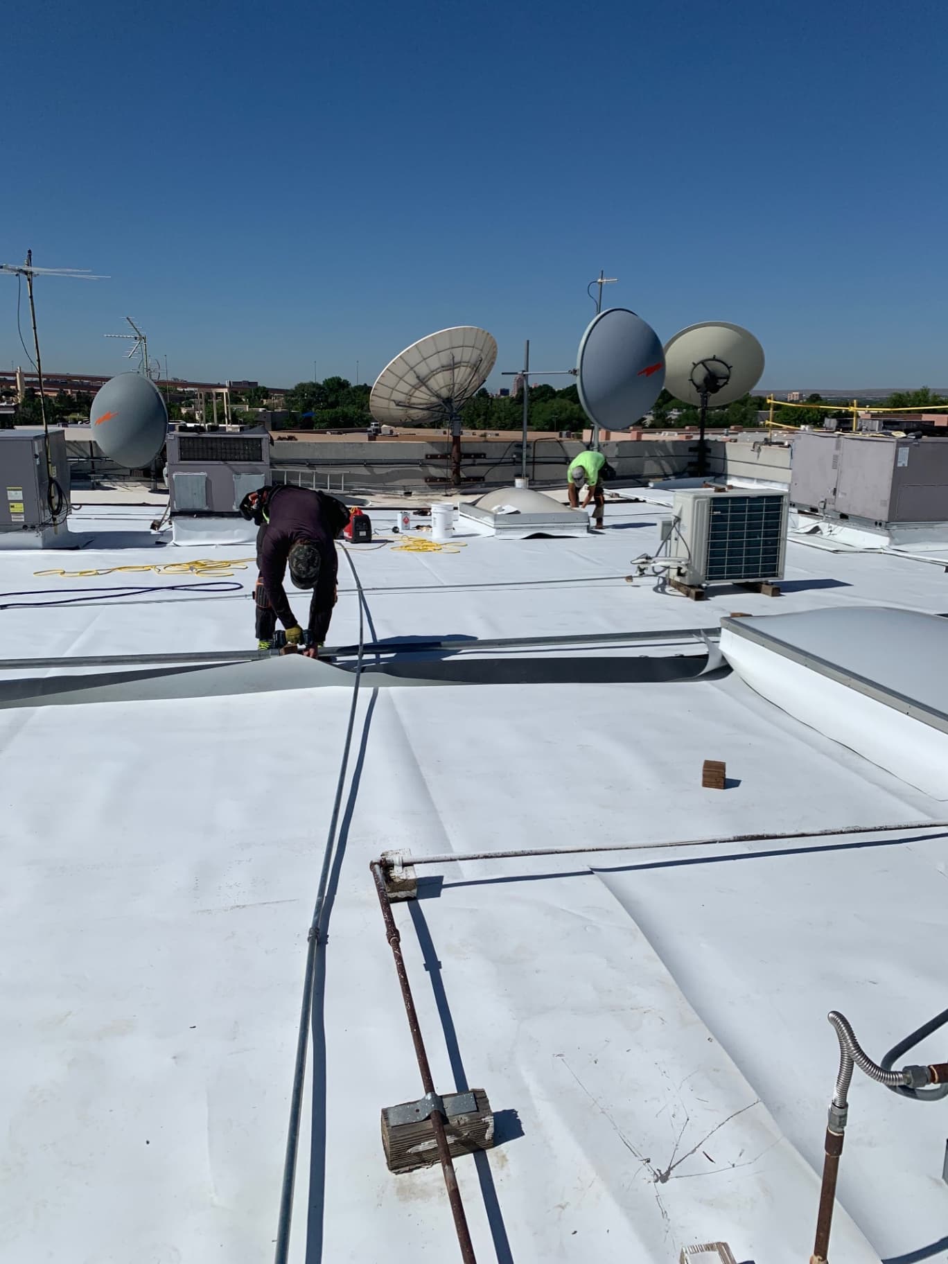 Mechanically attached TPO roofing being installed near rooftop satellite dishes and HVAC condenser