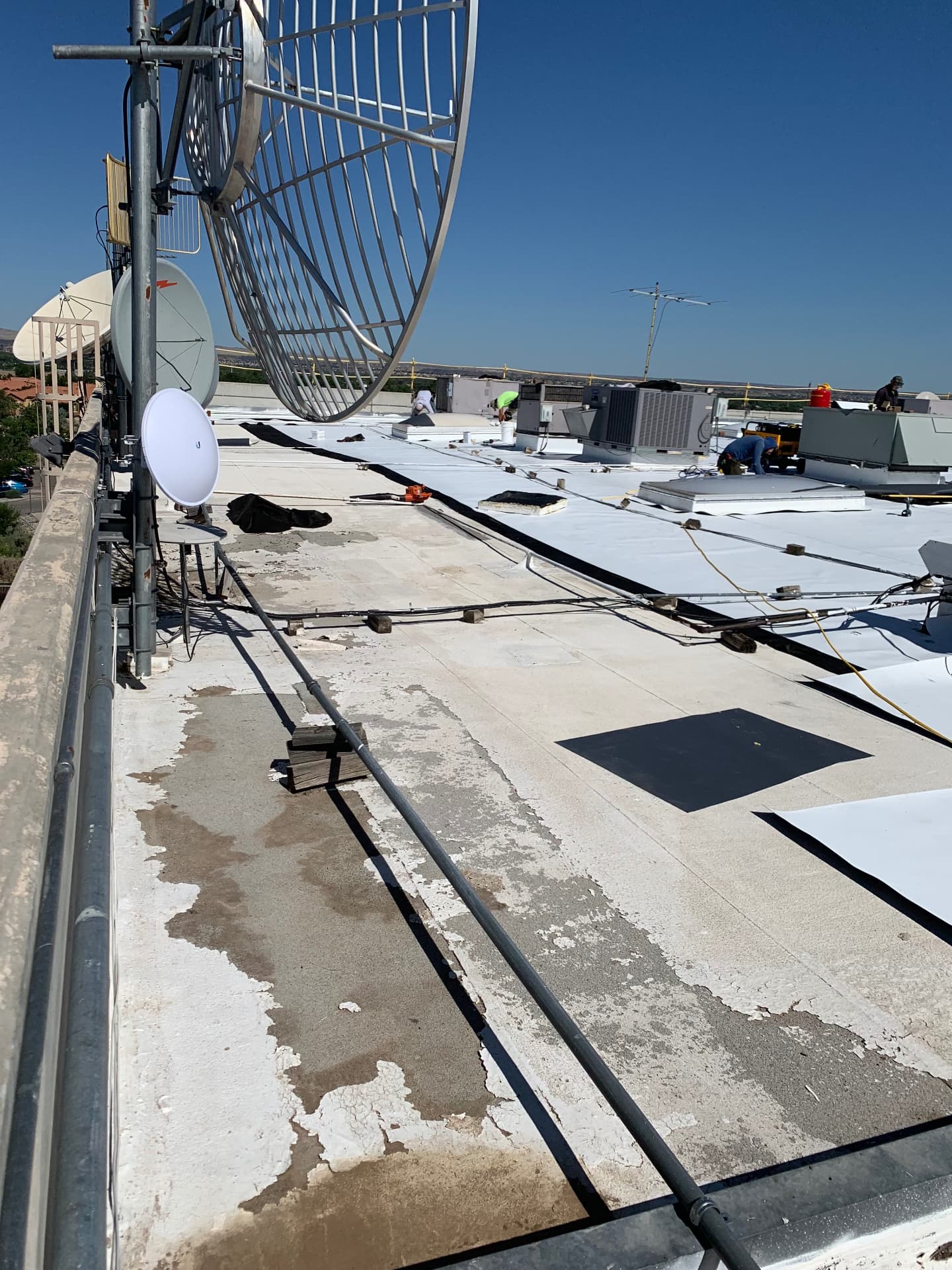 Commercial TPO roofing installation in progress around satellite dishes and rooftop equipment