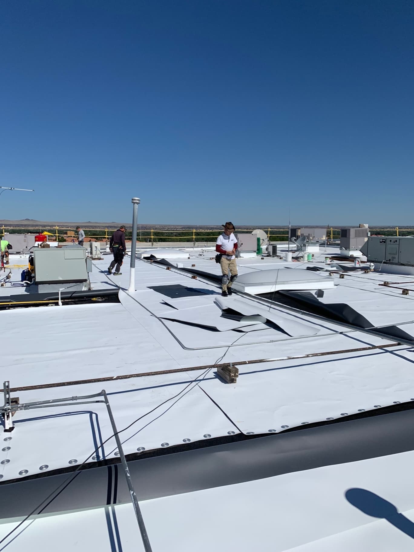 Crew installing TPO membrane across an expansive commercial rooftop with skylights and parapet
